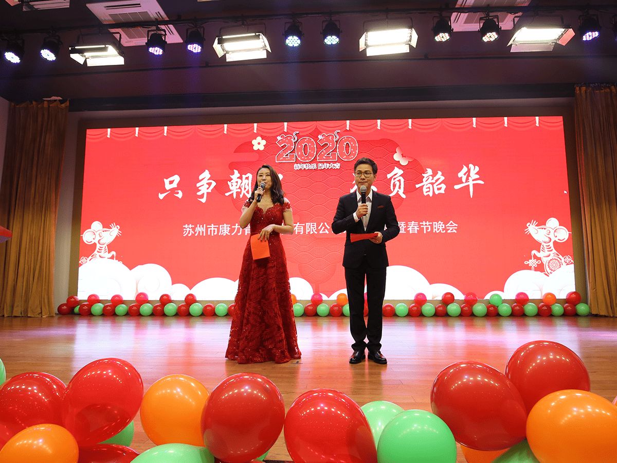 Two hosts on stage at Kangli's annual Spring Festival gala, framed by stage lights and red and green balloons