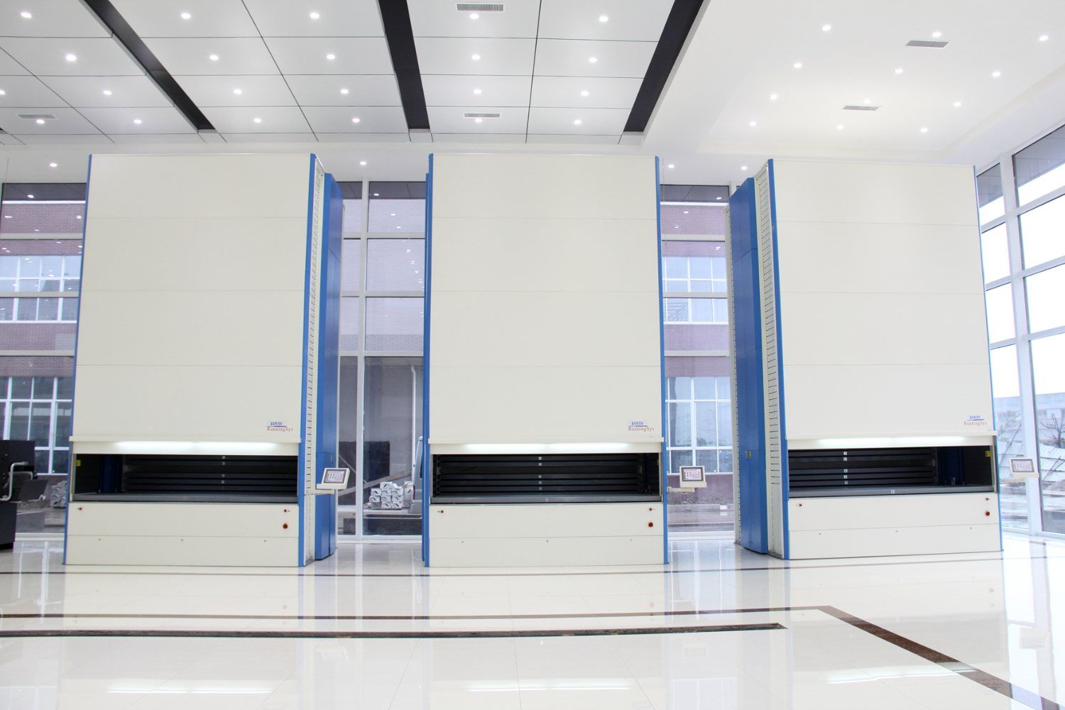 Three automated vertical storage carousels holding raw alloy stock in Kangli's material warehouse