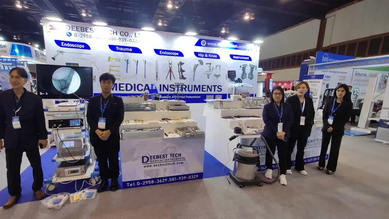 Medical-instrument exhibition stand with display trays and five participants wearing dark clothing and blue lanyards in the aisle.