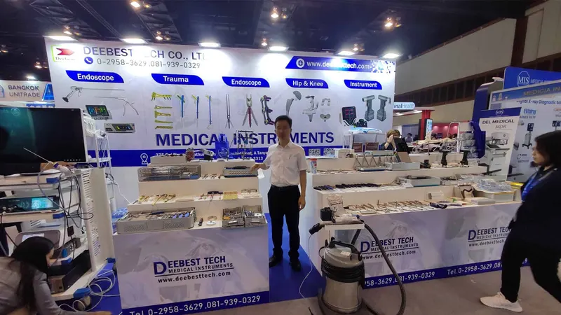 Deebest Tech exhibition stand with white-and-blue graphics, display counters, three foreground participants and several others behind the counters in an exhibition hall.