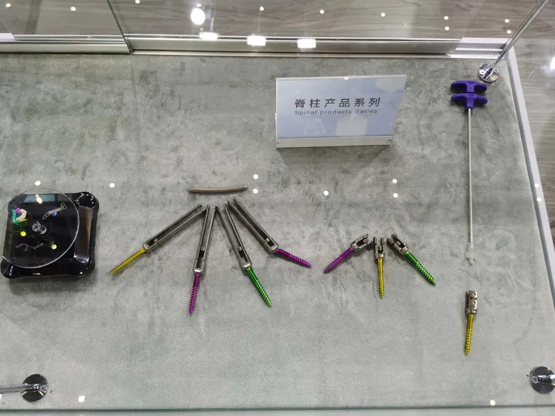 A glass case contains four matching spinal assemblies with coloured threaded pieces and additional metallic components beneath a sign reading “Spinal products series”.
