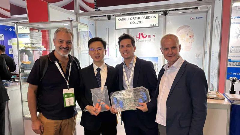 Four participants pose across the foreground of a branded exhibition booth, with display cabinets, printed backdrops and neighboring stands visible.