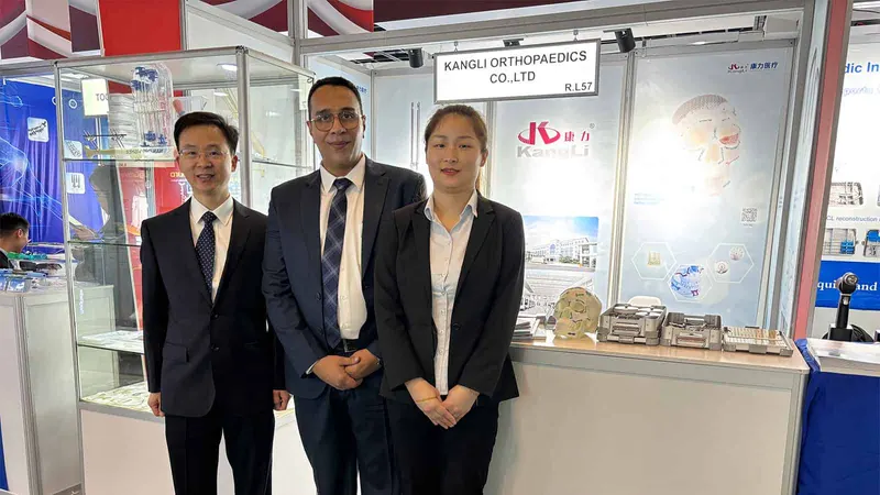 Three participants pose at an orthopaedic exhibition stand beside a glass display cabinet and product counter.