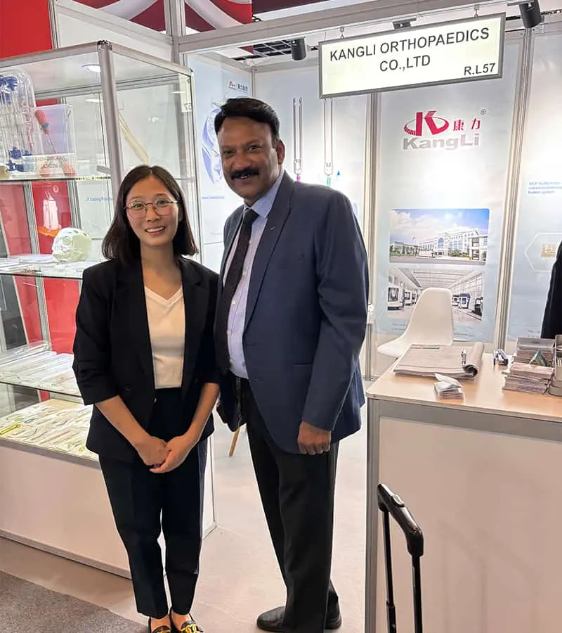 Two participants pose in front of glass display cabinets, white counters, printed panels and an overhead exhibition sign.