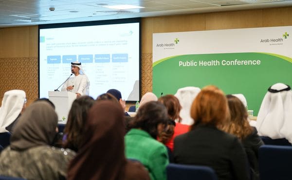 Public-health conference session with a speaker at a lectern, seated audience and projected presentation in a meeting room.