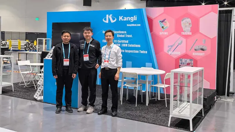 Three people stand in front of a blue and pink branded exhibition stand with a display cabinet, furniture, and a carpeted booth area.