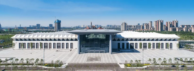 Conference centre with a tall glazed central entrance, projecting roof, white wings, and a few people in the forecourt.