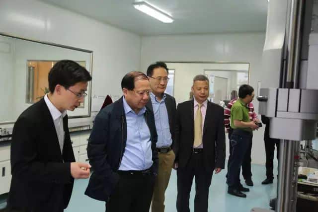 Seven people stand inside a white-panelled production or testing room beside large industrial equipment.