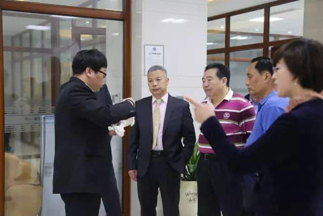 Five people stand in a corridor or reception area beside glazed rooms and interior windows.