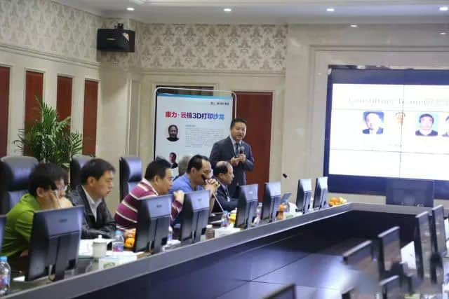 At least seven people sit in a conference room while one speaker addresses them with a handheld microphone.