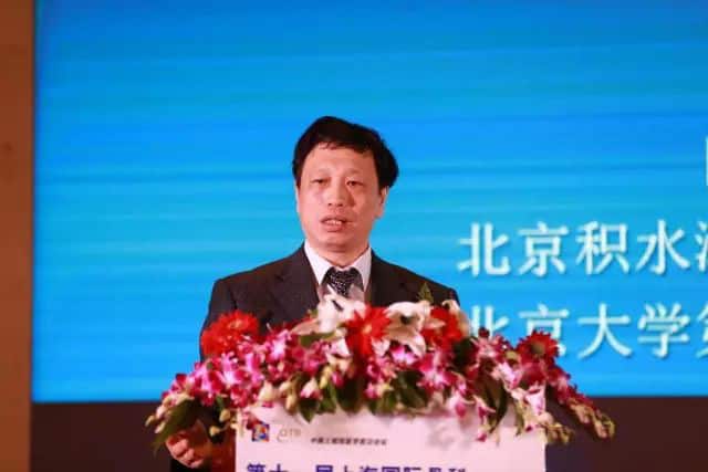 One suited speaker stands behind a flower-covered lectern in front of an illuminated blue stage backdrop.