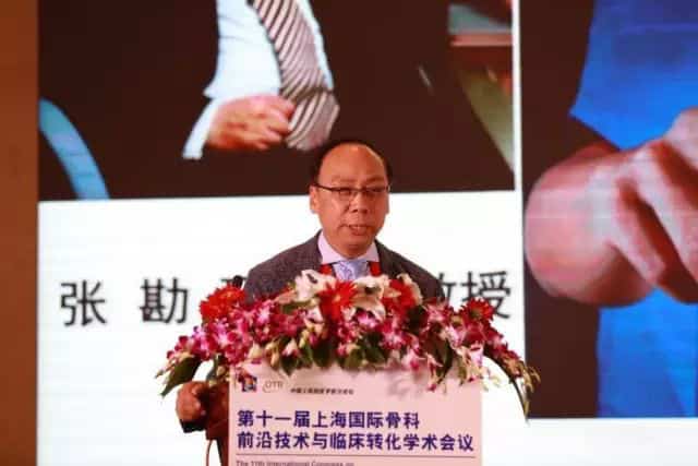 One speaker in a dark suit stands behind a flower-covered lectern with a large projected presentation screen behind.