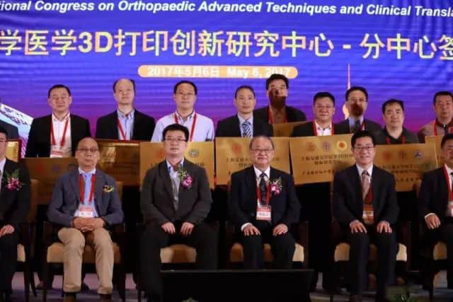 Sixteen participants pose in two rows on a raised stage, with coordinated plaques, formal clothing and a conference backdrop.