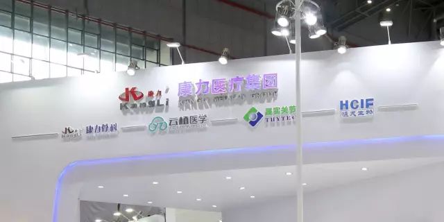 An empty white exhibition stand has a curved central opening, illuminated fascia and multiple group and subsidiary logos.