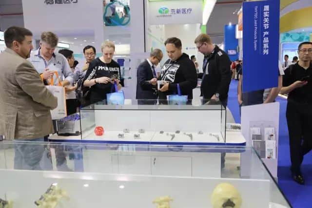 About ten participants gather at a medical-equipment exhibition stand with glass cases, hanging banners and a counter.