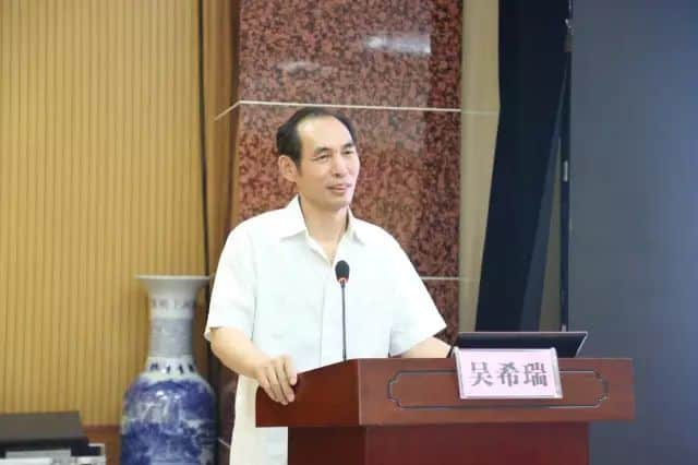 One participant in a white collared shirt stands behind a lectern with a gooseneck microphone and open laptop in an indoor speaking setup.