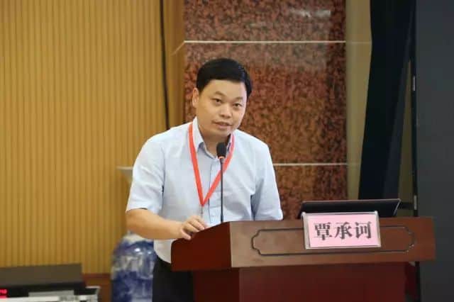 One participant in a light blue collared shirt stands at a lectern with a gooseneck microphone, laptop and pink name placard.