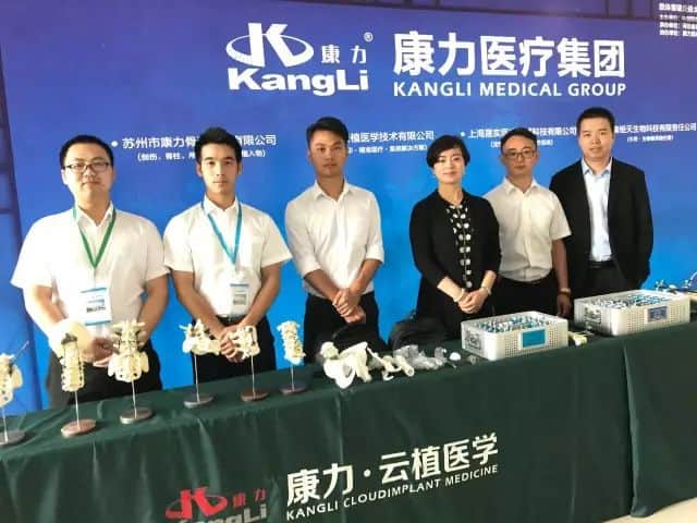 Six participants stand behind an exhibition table beneath a blue branded backdrop with a white logo and English Kangli Medical Group wording.
