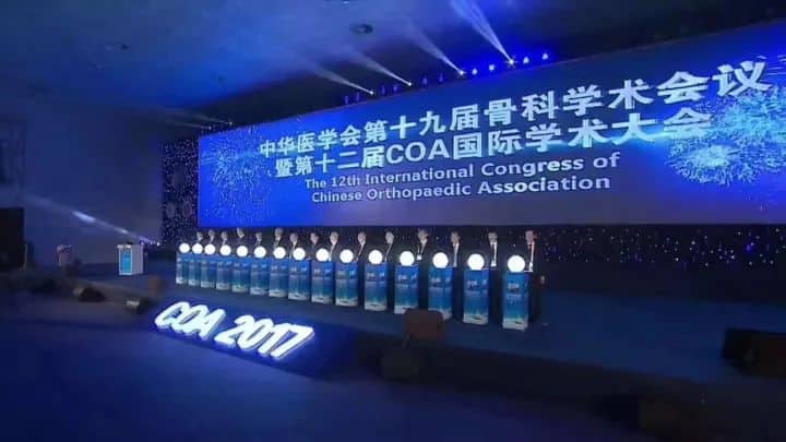 A stage with a blue LED congress backdrop, lectern and one indistinct participant at an indoor conference opening.