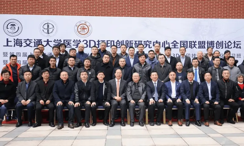 Approximately 40 workshop participants pose in three rows in front of a white event banner and red brick wall.