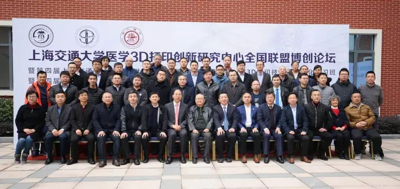 Approximately 45 participants pose in three rows outdoors in front of an event banner, with 16 people seated in the front row.