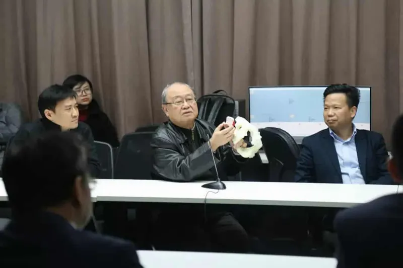 Seven participants sit around a conference table while one holds up a pale ring-shaped physical model.