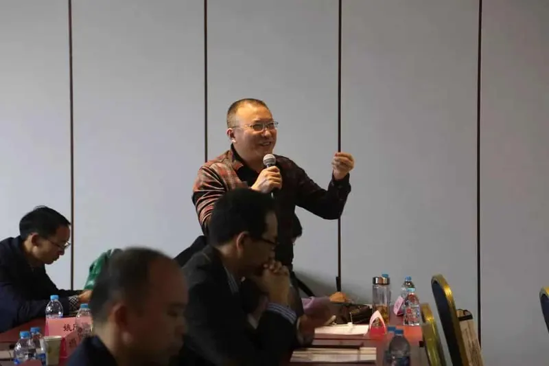 Four participants are visible in a workshop session, with one speaker standing and three attendees seated at tables.