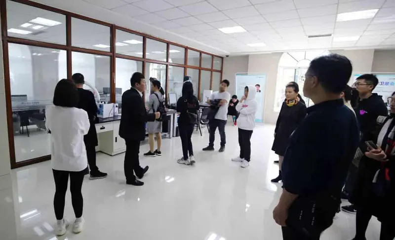 Eleven people stand and talk in a bright facility with glazed laboratory-style partitions and equipment.