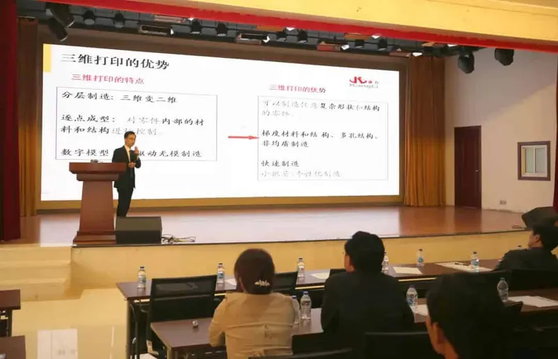 One speaker stands at a lectern before a projected slide while five audience members sit at tables in an auditorium.