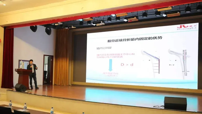 One speaker gestures toward a projected slide from a lectern on an auditorium stage.