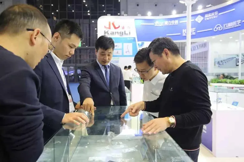 Five participants stand around a glass-topped display case at an exhibition stand, examining items inside.