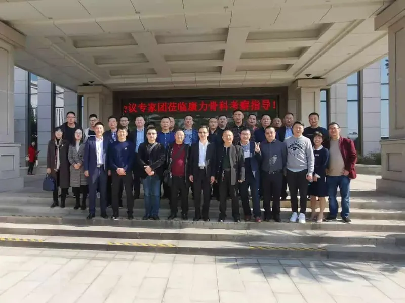 Approximately 30 participants pose in rows at a building entrance, with a red plant at the left.