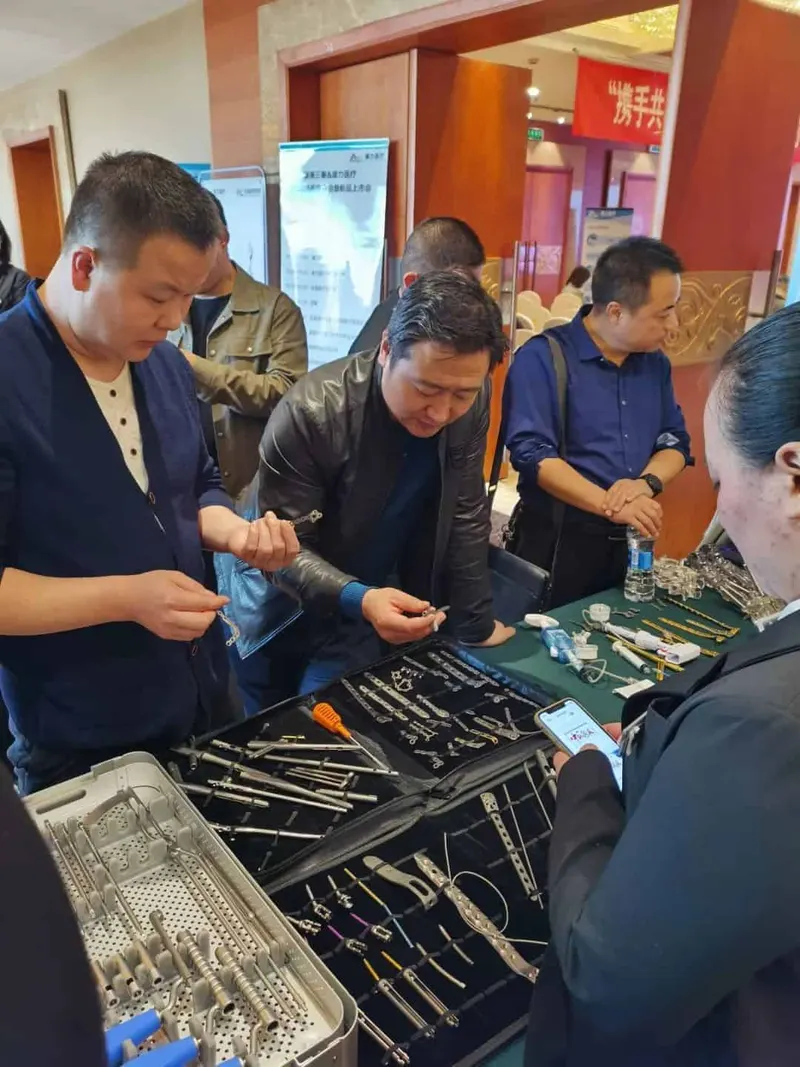 Seven people gather around tables while participants handle small metal components and instruments in an indoor lobby or conference area.