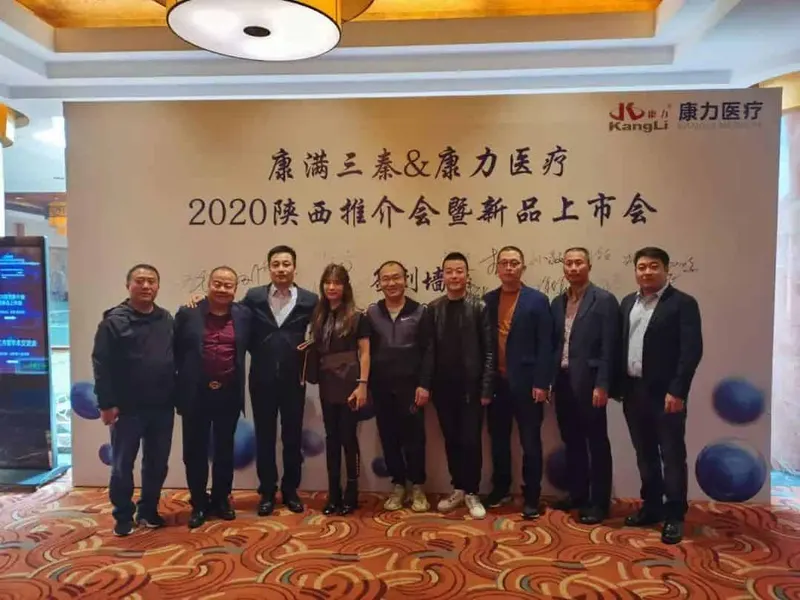 Nine participants stand in a line facing the camera before a printed event backdrop inside a hotel or conference venue.