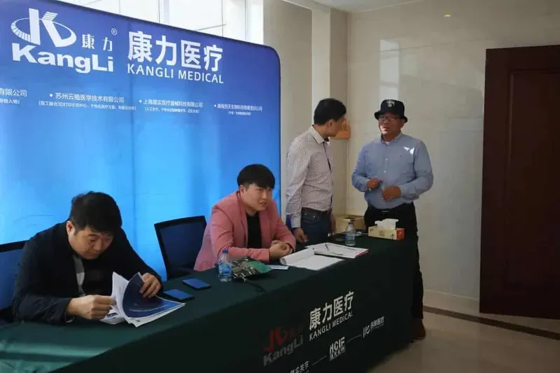 Four people gather around a staffed registration table with booklets, papers and bottled water beneath a large blue event backdrop.