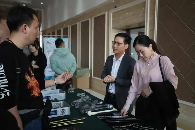 About six people gather around a table of medical-device components beneath a presentation banner, including one person holding a small metallic component.