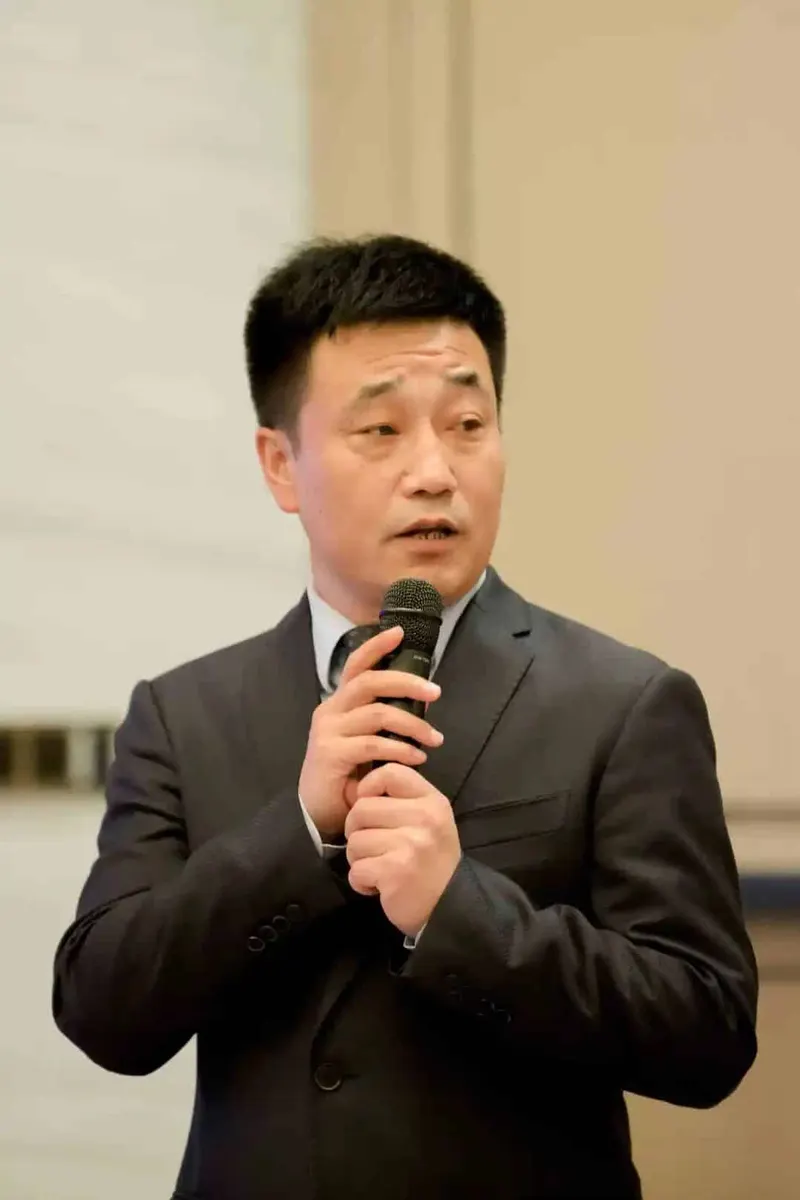 One participant in a dark suit holds a handheld microphone in an indoor event venue.