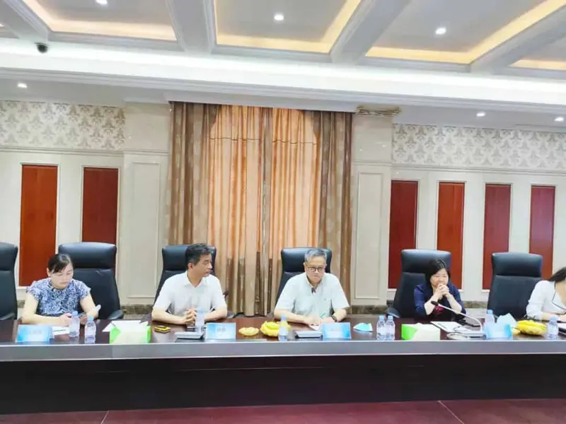Five participants sit behind a long conference table with microphones, papers, name cards, bottled water and refreshments.