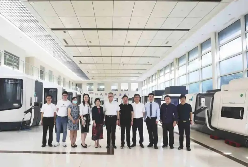 Eleven participants stand in a row near enclosed machines inside a bright industrial workshop.