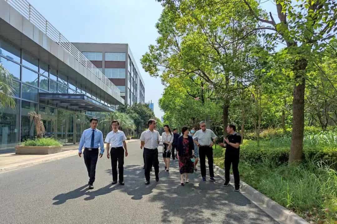 Seven people walk along a paved path beside a modern building with mature landscaping.